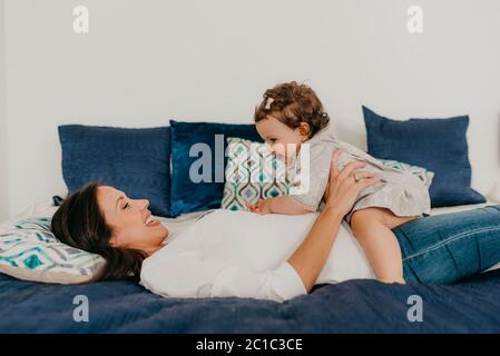 la giovane bella madre gioca con la figlia a letto a casa Foto Stock