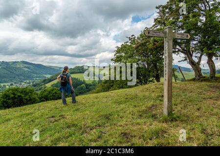 Una donna che guarda attraverso la Club Valley sul sentiero a lunga distanza Offaa's Dyke. Un cartello con il dito che indica il punto intermedio della passeggiata. Foto Stock