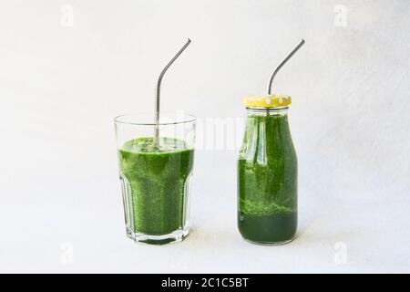 Frullato verde con spinaci in bottiglia piccola e in bicchiere da bere con paglia metallica. Spazio di copia per il testo. Concetto di stile di vita sano Foto Stock