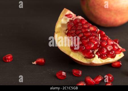 Melograno fetta di frutta e semi di vita ancora rustico sfondo nero Foto Stock