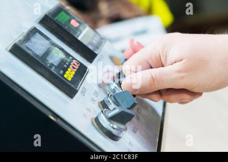 Un primo piano della mano di un uomo tiene un interruttore rotante sul pannello di controllo dell'attrezzatura con strumenti. Foto Stock