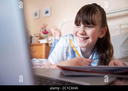 Giovane ragazza sdraiata sul letto in camera con laptop di studio e la scuola domestica Foto Stock