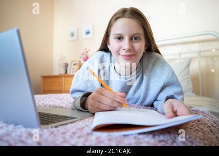 Ritratto di ragazza teenage che si trova sul letto in camera da letto con laptop di studio e la scuola di casa Foto Stock