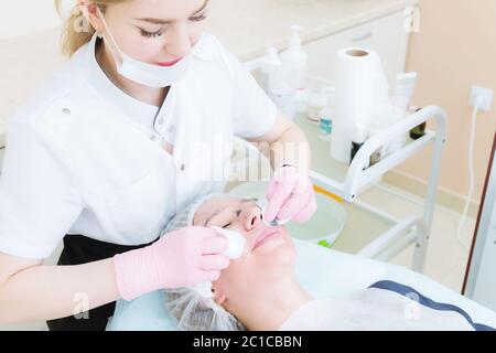 Un primo piano della procedura di pulizia nell'ufficio di cosmetologia. Le mani del cosmetologo in guanti rosa vengono rimosse Foto Stock