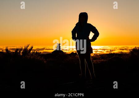 Silhouette ragazza in controluce sulla cima della montagna al tramonto Foto Stock