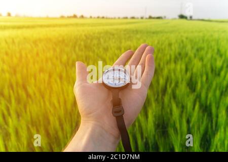 Trovare una direzione in natura su un campo di grano. La mano di un uomo tiene una bussola Foto Stock