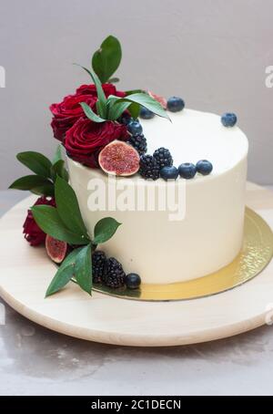 Elegante torta nuziale decorata con rose rosse fresche, foglie verdi, fichi e mirtillo. Sfondo grigio chiaro. Foto Stock