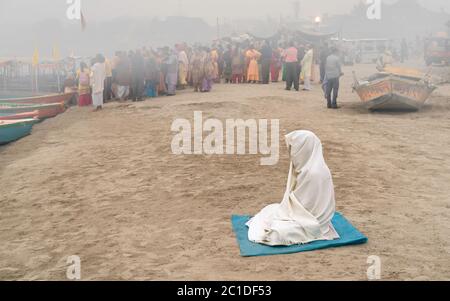 Solitaria donna indù coperta in scialle profonde nella mediazione sulla riva del fiume Jamuna all'alba. Foto Stock