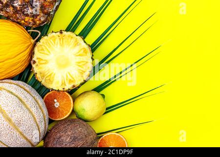 Estate creativo tropico fuit layout. Ananas, melone, limone, arancia, cocco e foglia di palma su sfondo giallo. Foto Stock