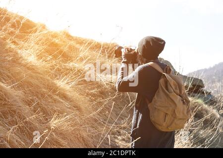 Donna hipster-fotografo con fotocamera dslr scattare foto . Ragazza elegante in occhiali da sole con una macchina fotografica sulla natura Foto Stock