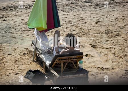 Un turista seduto sulla spiaggia di Goa che scribbe attraverso il suo diario. Foto Stock