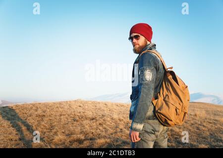 Ritratto di moda di un giovane hipster con bearded che indossa occhiali da sole, uno zaino e un cappello su uno sfondo con copyspase nel mou Foto Stock