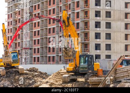 Escavatori con benne rialzate sullo sfondo di un edificio residenziale a più piani in costruzione Foto Stock