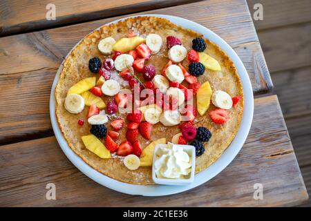 Grande pancake con frutta estiva e panna montata su un tavolo di legno. Vista dall'alto. Foto Stock