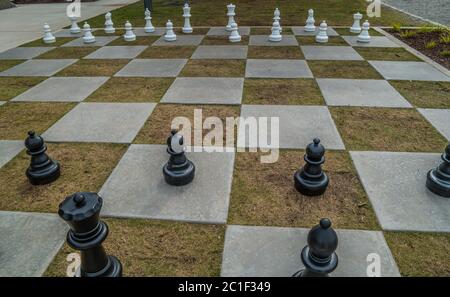 Guardando verso il basso un gigante scacchi all'aperto set su cemento e piazze d'erba per spostare i grandi pezzi di gioco Foto Stock