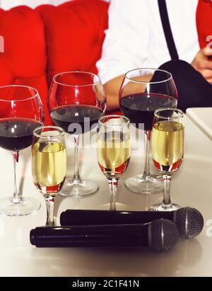 Vino bianco e rosso, bevanda alcolica, bevanda, servita in diversi bicchieri e due microfoni wireless sul tavolo bianco Foto Stock