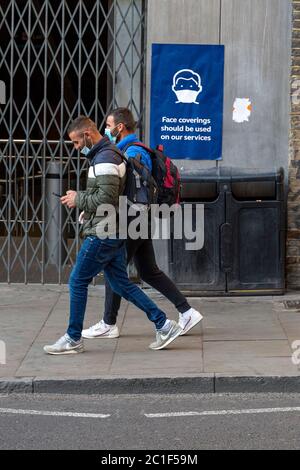 Due giovani uomini che passano davanti a un avviso fuori dalla stazione di London Bridge informando le persone che le maschere facciali dovrebbero essere indossate sui treni. Segretario di Stato per i trasporti Grant Shapps, Ha annunciato che tutti i passeggeri devono indossare maschere facciali sui trasporti pubblici a partire dal 15 giugno e ha avvertito che l'uso di una maschera facciale sarebbe una condizione per viaggiare e la mancata osservanza di tali norme comporterà il mancato viaggio o l'inadempimento di una sanita. Foto Stock