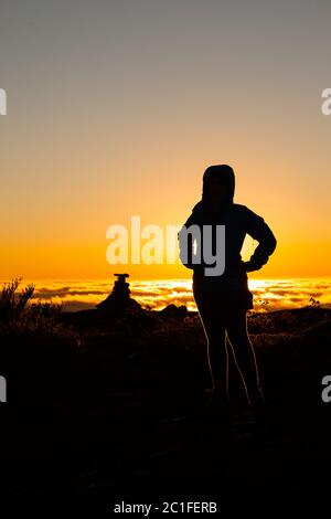 Silhouette ragazza in controluce sulla cima della montagna al tramonto Foto Stock