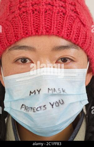 Donna asiatica con la mia maschera ti protegge scritto in marker sulla sua maschera facciale Foto Stock
