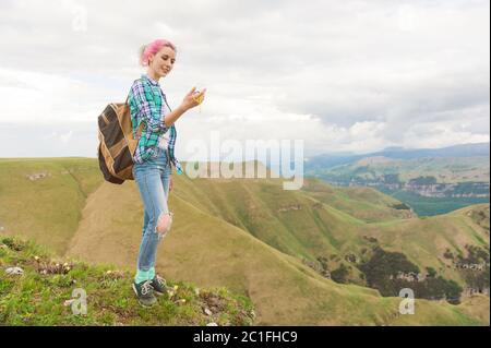 Una ragazza hipster viaggiato da un blogger in una camicia plaid e con capelli multicolore utilizzando una bussola in piedi su un plateau backgrou Foto Stock