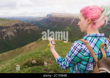 Una ragazza hipster viaggiò con un blogger in una camicia plaid e con capelli multicolore usando una bussola sullo sfondo nel bac Foto Stock