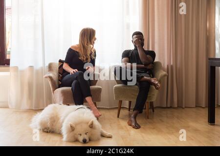 Uomo e donna che discutono seduti sulle poltrone del soggiorno con il cane che dormiva davanti. Foto Stock