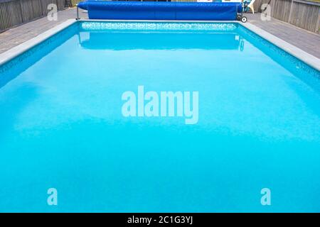 Moderna piscina con copertura per la protezione dello sporco arrotolata e scala in giardino. Foto Stock