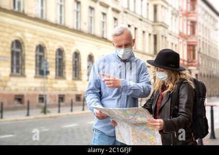 Un uomo dai capelli grigi in una camicia in denim mostra la direzione a una ragazza giovane. Stanno guardando la mappa. Maschere sui loro volti. La ragazza indossa un buio Foto Stock