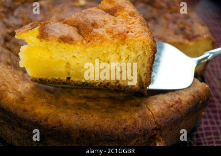 Torta su una tovaglia di colore borgogna. Un pezzo di torta viene preso con una spatola Foto Stock