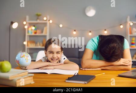 Lavoro di stress con i bambini in ufficio domestico. Madre stanca che dorme su una figlia malvagia del desktop guardando la macchina fotografica in ufficio domestico. Foto Stock