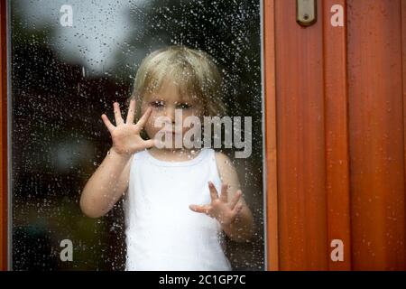 Triste bambino dietro la finestra in una giornata piovosa Foto Stock