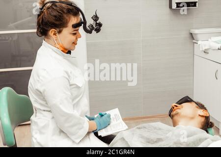 Giovane donna dentista medico sul posto di lavoro conduce un'indagine paziente. Storia presa. Attrezzature per il luogo di lavoro per il settore sanitario per un medico. Odontoiatria Foto Stock