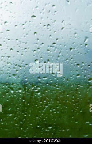 Lo sfondo naturale cade su entrambi i lati del vetro dalla pioggia e dalla vista astratta di appannamento, gocce di pioggia contro il blu Foto Stock