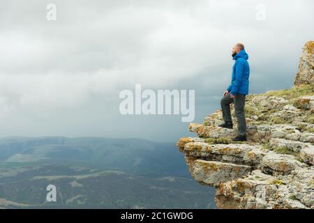 uomo turistico hipster bearded che si erge sul bordo di una roccia e che guarda fuori in lontananza su un altopiano epico. Il concetto di Foto Stock