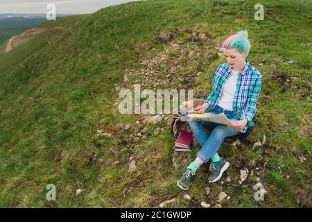 Ragazza viaggiatore con capelli multicolore seduto sulla carta da lettura natura e tenendo una bussola in mano. Il concetto di navigazione th Foto Stock