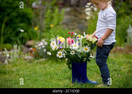 Bambino che tiene stivali di gomma con fiori belli in giardino Foto Stock