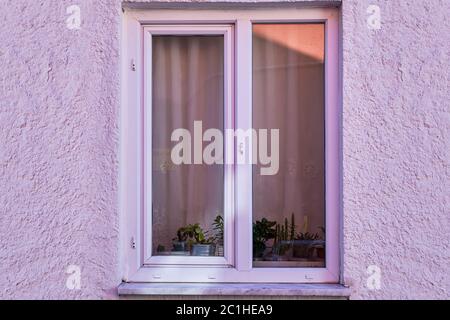 Frammento della facciata di una villa di campagna con una finestra in plastica color lilla e parete intonacata con stucco grezzo dipinto in viola. Foto Stock