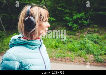 Ritratto di una bella ragazza sportiva bionda in una giacca leggera running down vestendo le cuffie bluetooth con la musica o il sostantivo Foto Stock