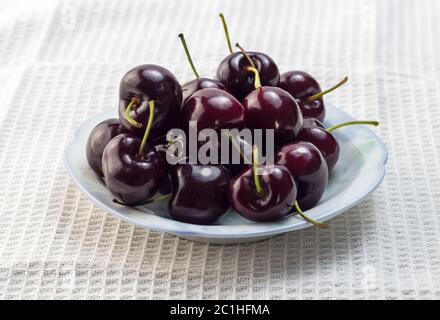 Mature amarene in un piccolo recipiente isolato sul panno bianco sullo sfondo Foto Stock