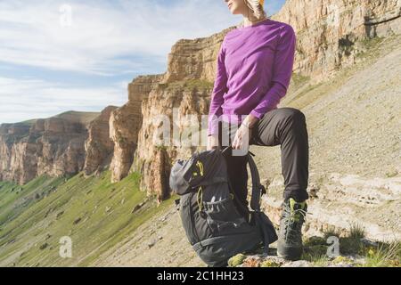 Sorridente viaggiatore ragazza in un cappello giallo e un paio di occhiali da sole si erge ai piedi di epiche rocce con uno zaino successivo e sembra un Foto Stock