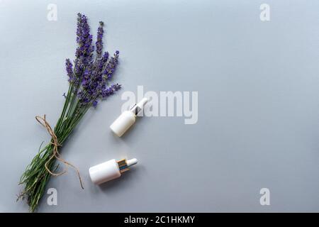 Due bottiglie di siero cosmetico senza brandello e mazzetto di lavanda su sfondo grigio. Vista dall'alto, disposizione piatta, spazio per la copia. Foto Stock