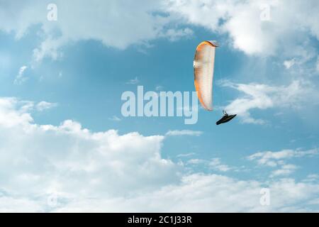 Il parapendio professionista vola su un parapendio bianco contro il cielo blu e le nuvole bianche. Sport di parapendio Foto Stock