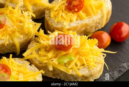 Formaggio cheddar grattugiato e pomodori ciliegini su fette di baguette primo piano Foto Stock