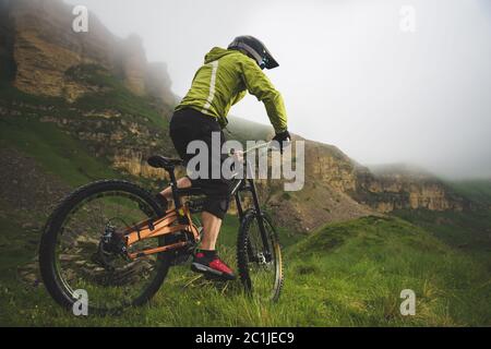 Un uomo in un casco di montagna che cavalcano una mountain bike gira intorno alla natura bella in tempo nuvoloso. Discesa Foto Stock