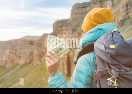 Una ragazza viaggiatore che indossa un cappello e occhiali da sole sta tenendo un centinaio di dollari bollette nelle mani di un ventilatore contro lo sfondo di cli Foto Stock