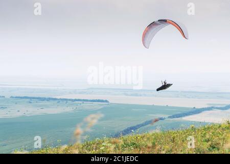 Parapendio bianco arancio con parapendio in bozzolo sullo sfondo di campi del cielo e nuvole. Parapendio Sport Foto Stock