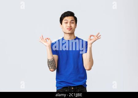 Emozioni diverse, stile di vita della gente e concetto di pubblicità. Ragazzo cheeky bello queer, gay asiatico uomo in t-shirt blu rimanere calma e paziente, tenere Foto Stock