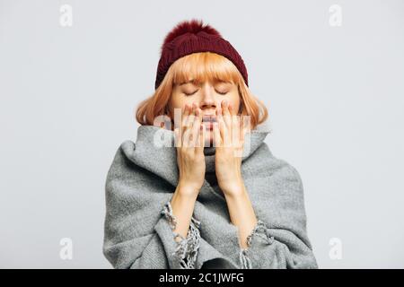 Cute femmina malsana in cappello rosso, avvolto in sciarpa caldo starnuti, sperimenta sintomi allergici, ha catturato un freddo, chiuso eyes.Sick donna disperata ha fl Foto Stock