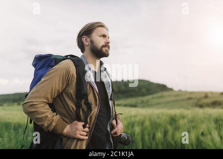 Vista laterale del fotografo bearded che si erge tra il campo verde Foto Stock