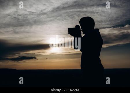 Uomo in silhouette con fotocamera per scattare foto del tramonto Foto Stock